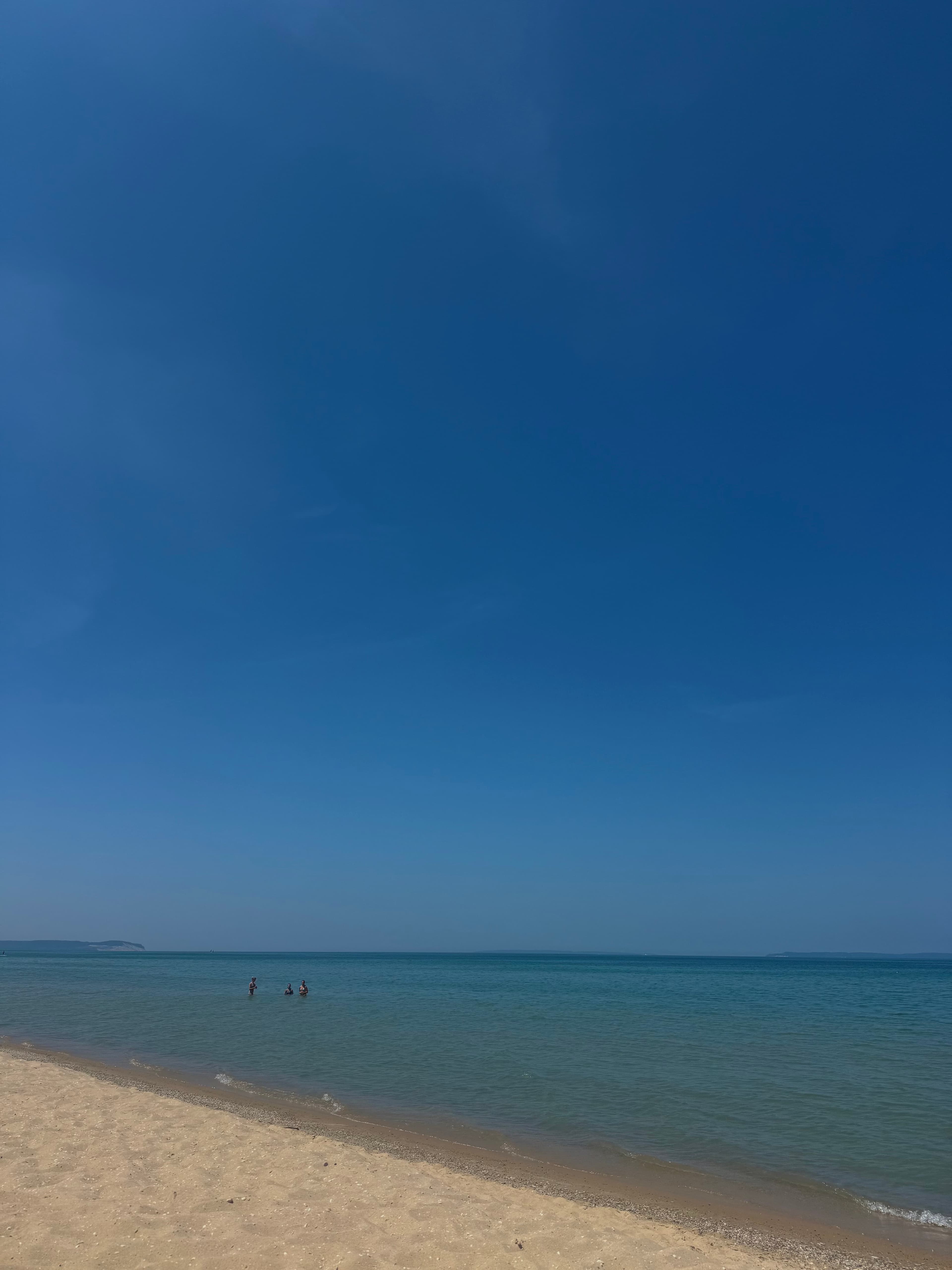 A calm Lake Michigan shoreline in Traverse City, with people wading in the turquoise water under a clear blue sky