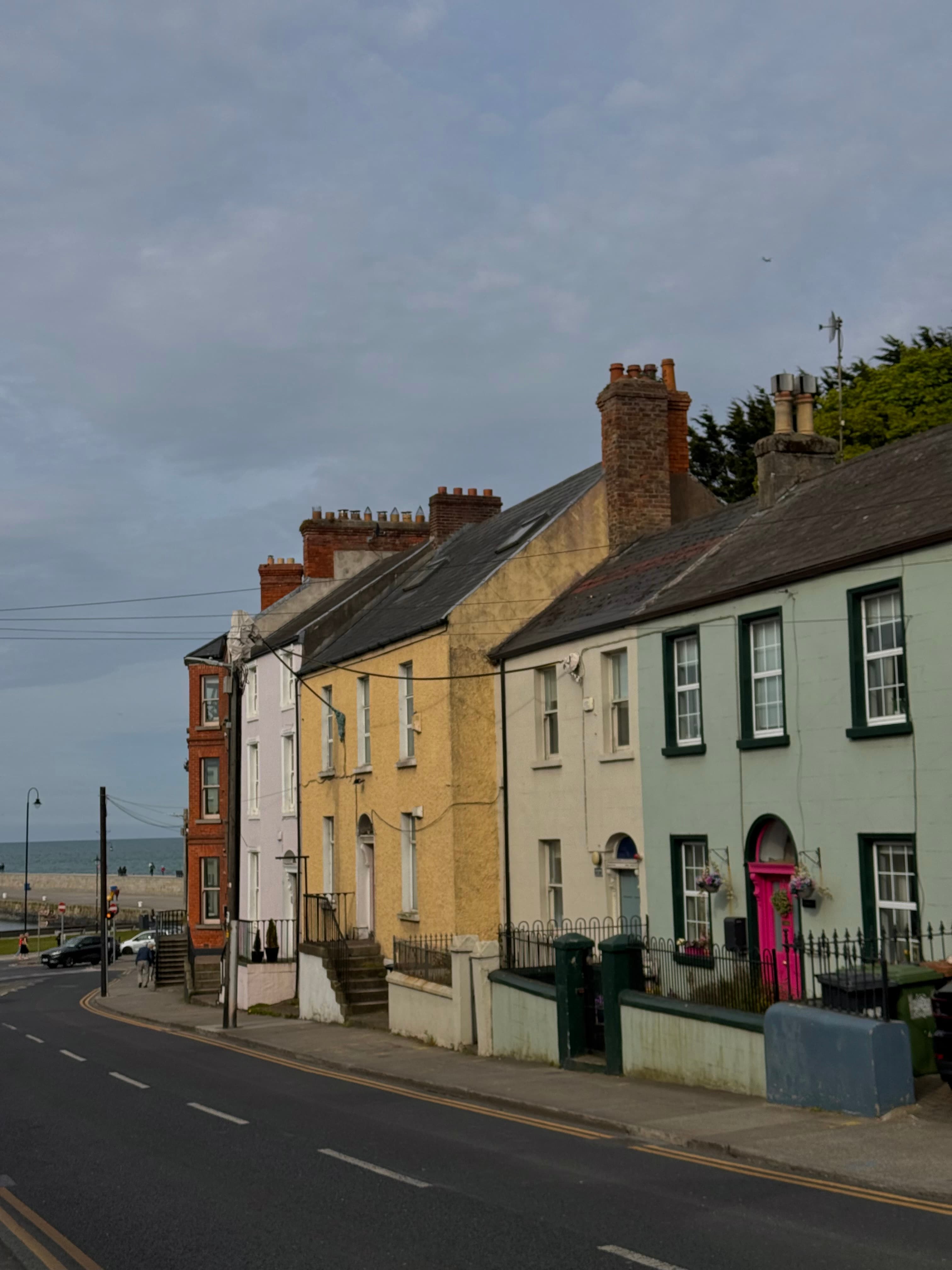 A row of colorful Irish terrace houses in white, yellow, and mint green along a coastal street