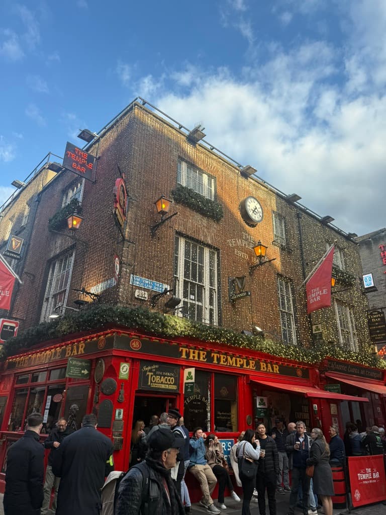 The exterior of The Temple Bar pub in Dublin, strung with lights and surrounded by a crowd